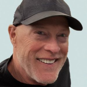 Smiling older man in a black cap and jacket.